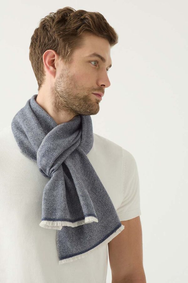 Man wears a cashmere scarf by KASMIRI around his neck to keep him warm and featuring a herringbone pattern with white fringing
