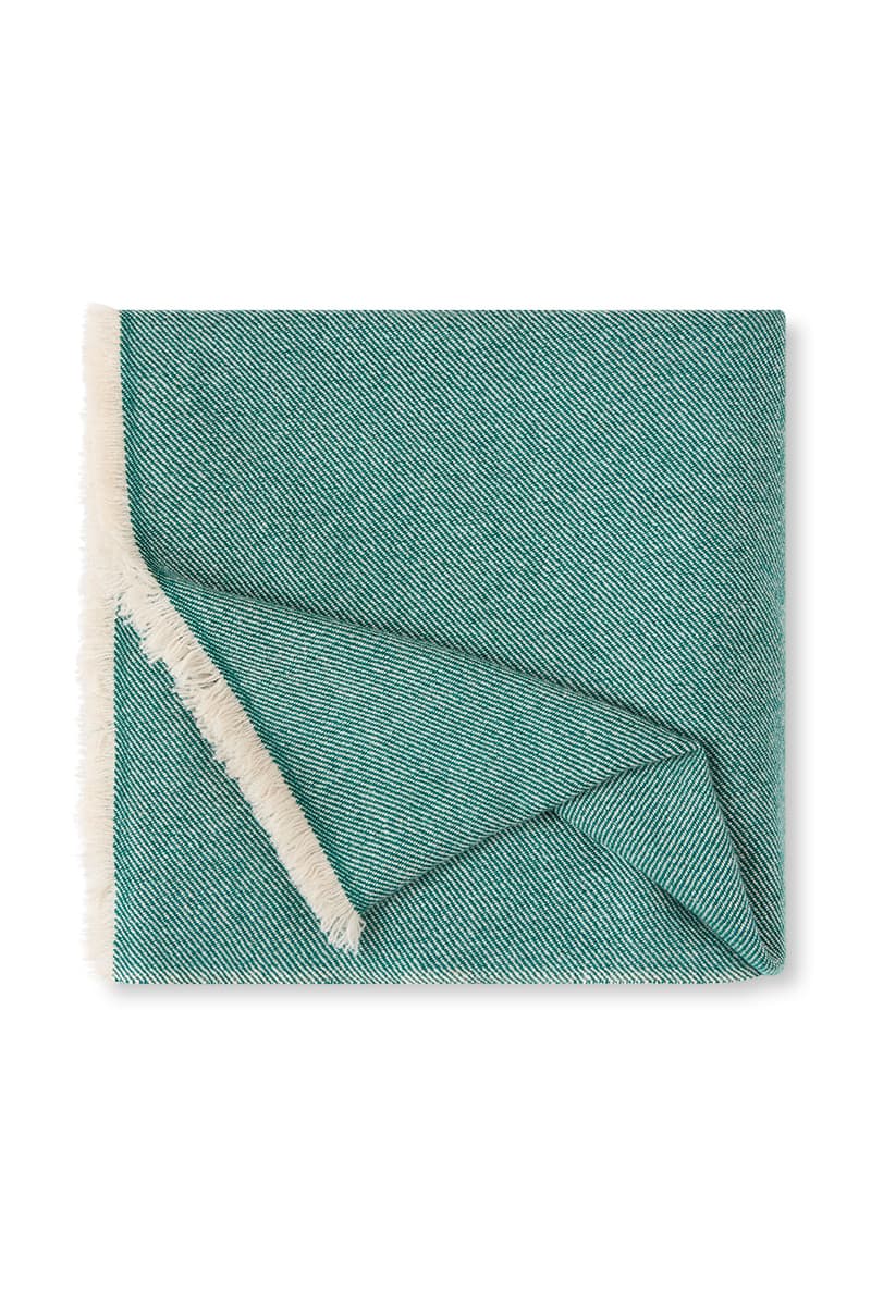 A folded cashmere throw blanket in Emerald Green handwoven in a diagonal weave and finished in soft fringing on either side.