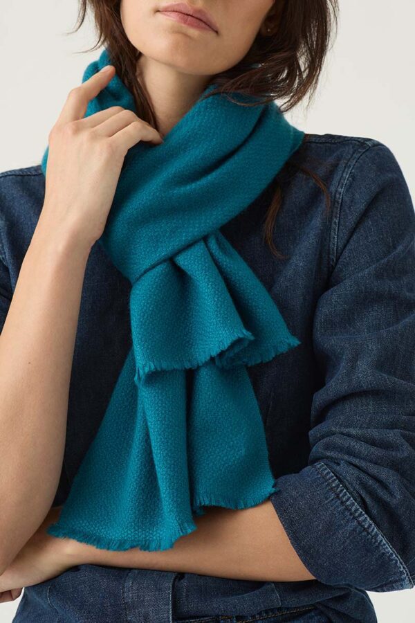 The Gatsby Cashmere Scarf worn around woman's neck in peacock